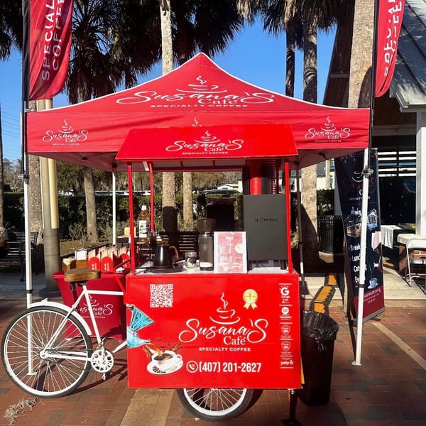 Susana's Cafe red coffee cart with a matching tent and flags under palm trees.