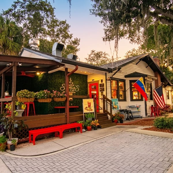 Savana's Cafe exterior with a red door, outdoor seating, and flags under a sunset sky.