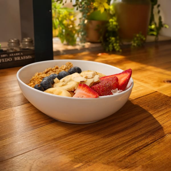 Bowl of granola topped with blueberries, banana slices, strawberries, almonds, and coconut on a wooden table.